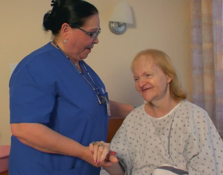 Una cuidadora de MJHS le toma la mano a una paciente mayor