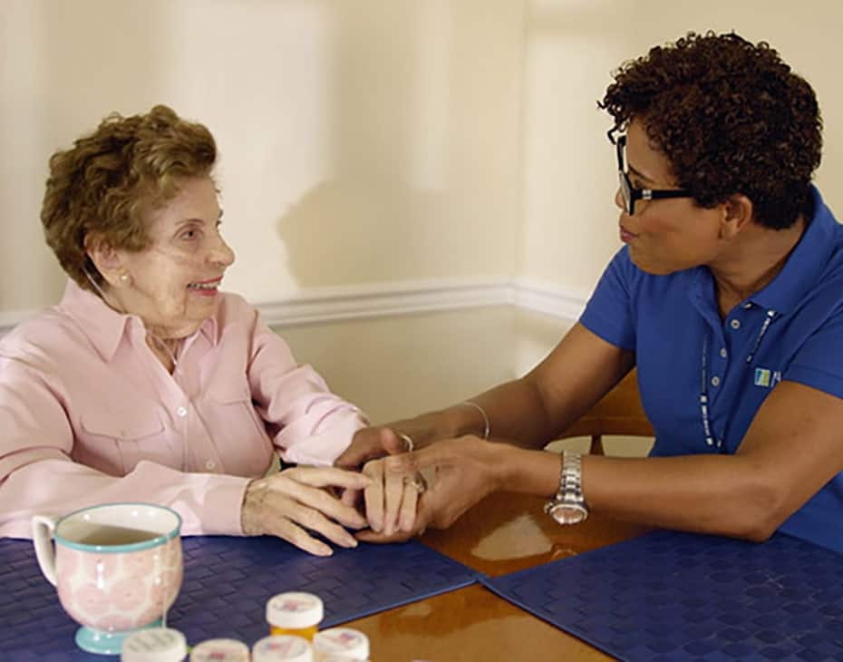 Una cuidadora del sistema de salud de MJHS contenta con una residente mayor al lado de una tetera