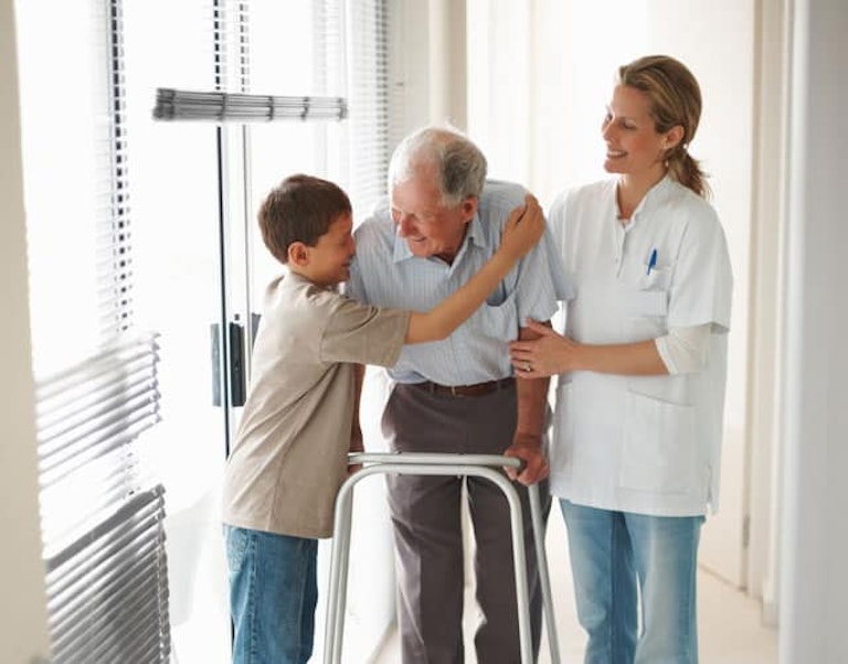Una cuidadora sonríe mientras un niño abraza a un paciente mayor