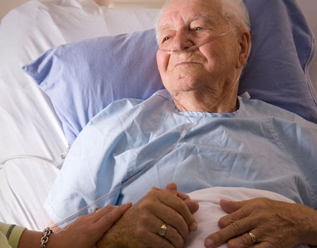 Una paciente en la cama de un hospital tomado de la mano con una mujer