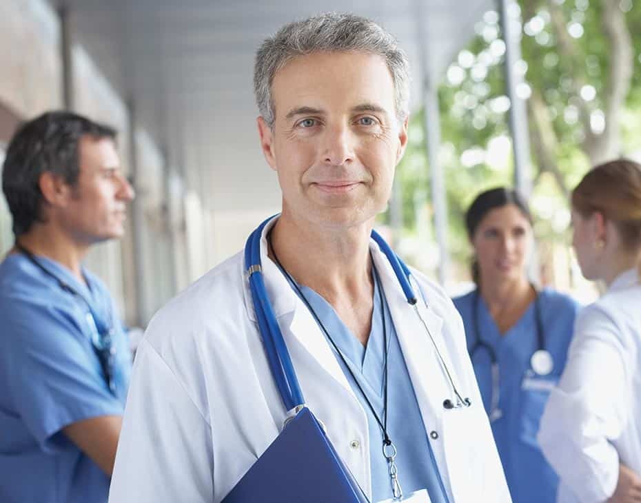 Un médico sonríe mientras enfermeros tienen una conversación en segundo plano