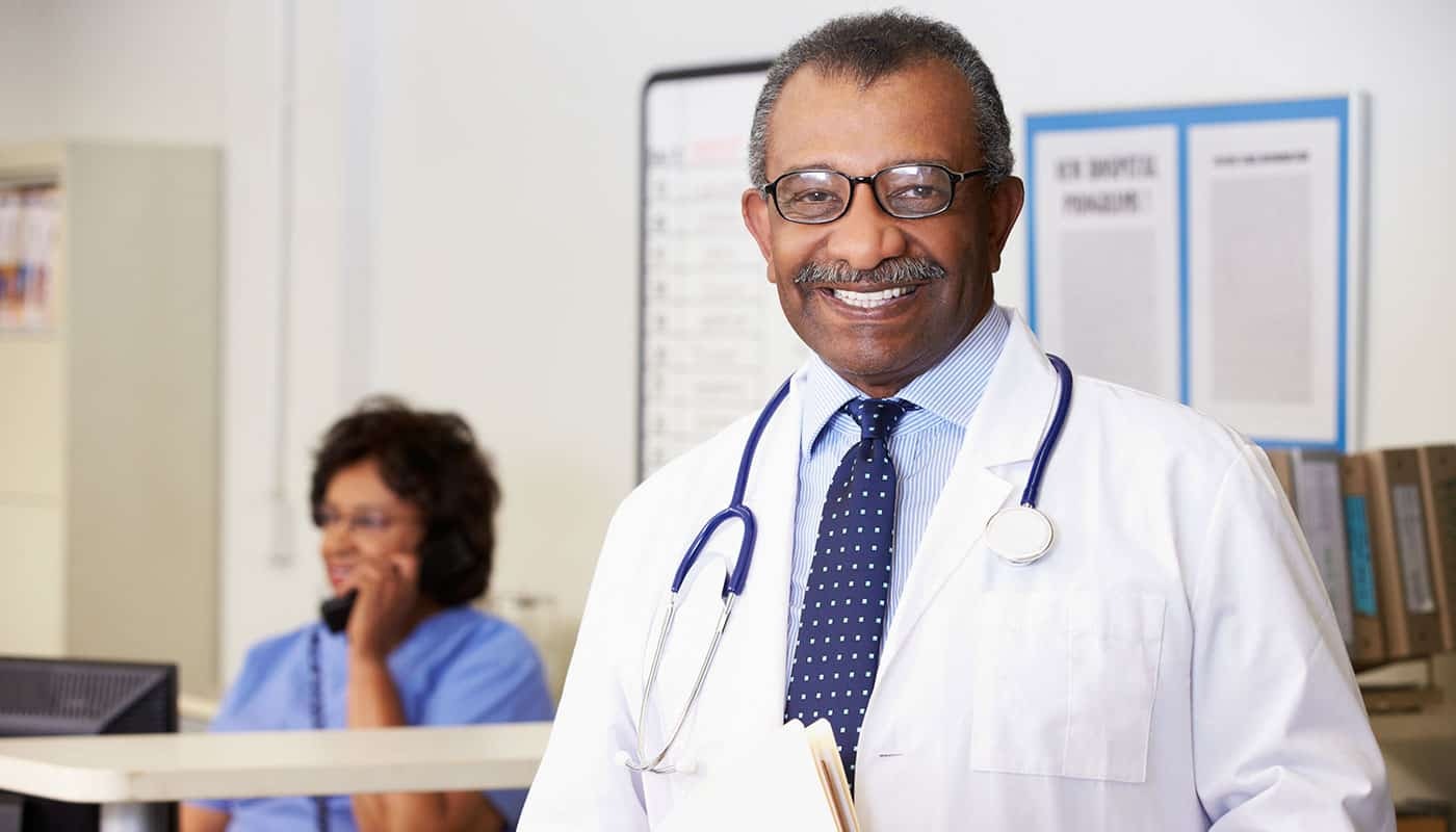 Portrait Of Smiling Doctor At Nurses Station as Nurse Speaks on Phone