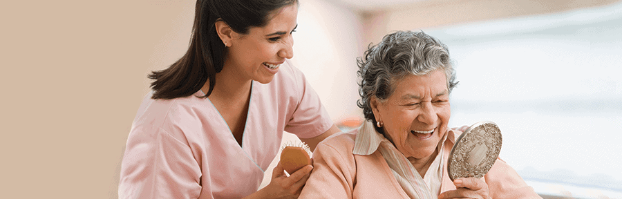 Enfermera sonriente le ayuda a una paciente mayor a peinarse el cabello