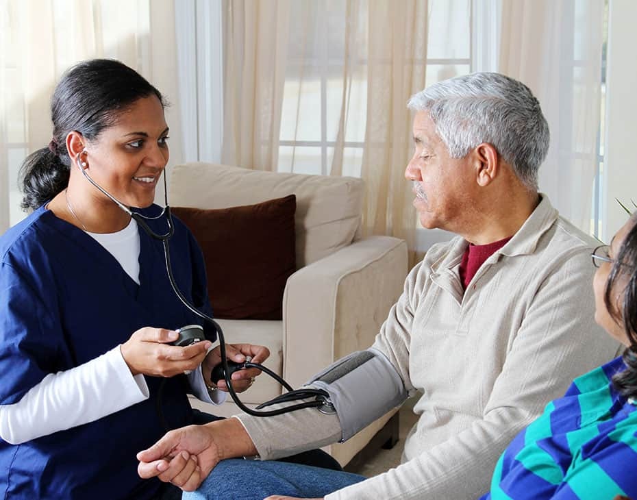 Cuidadora en el hogar le toma la presión arterial a un hombre mayor con su pareja a su lado
