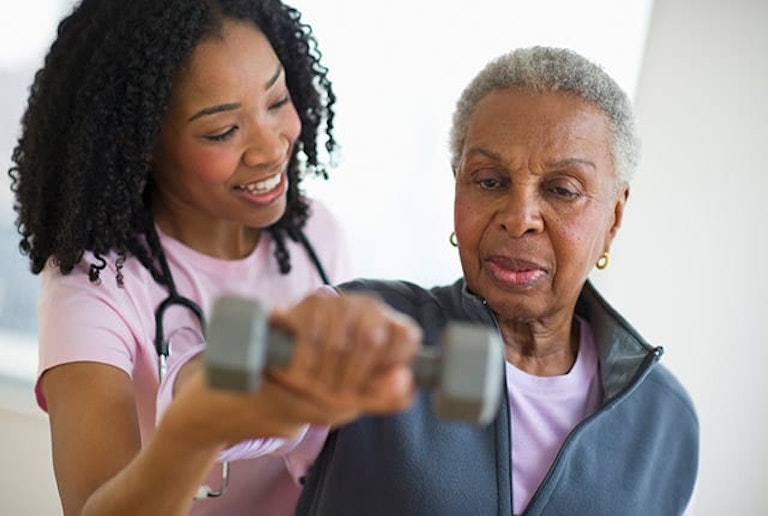 Smiling Nurse Helping Senior with Therapy by Using Dumbbell Exercise