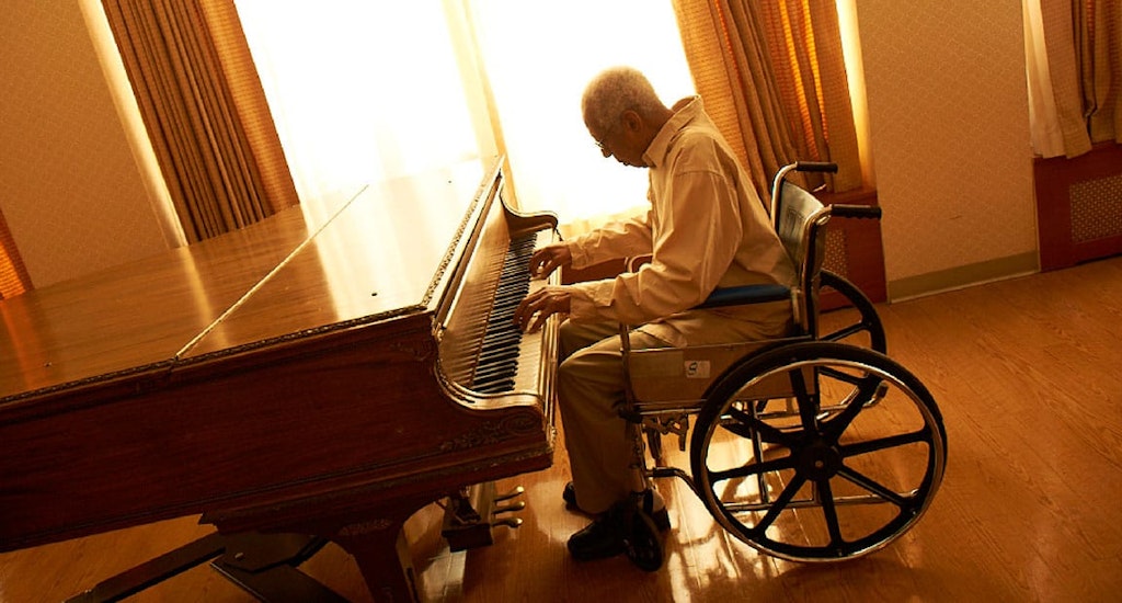 Un hombre mayor paciente a largo plazo toca el piano en una silla de ruedas