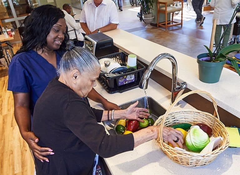 Una cuidadora de MJHS ayuda a una paciente mayor a lavar verduras