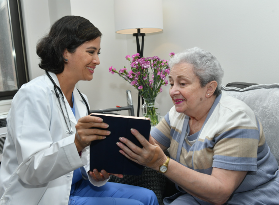 Older woman sitting on couch reading a book with a nurse