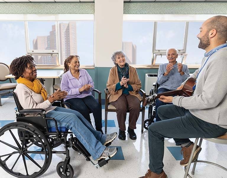 Elderly people applauding rhythmically while the musical therapist plays an instrument.