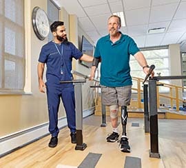 A physical therapist using a walking bar to help a man who has a prosthetic leg.